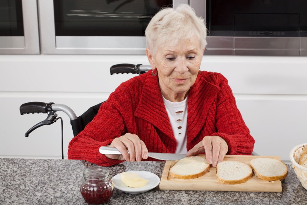 Eldre dame som smører sine skiver til frokost sittende i rullestol